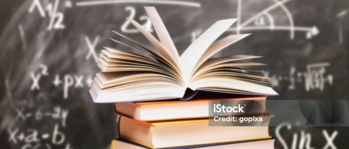 Opened book on a stack in front of a blackboard with mathematical formulas